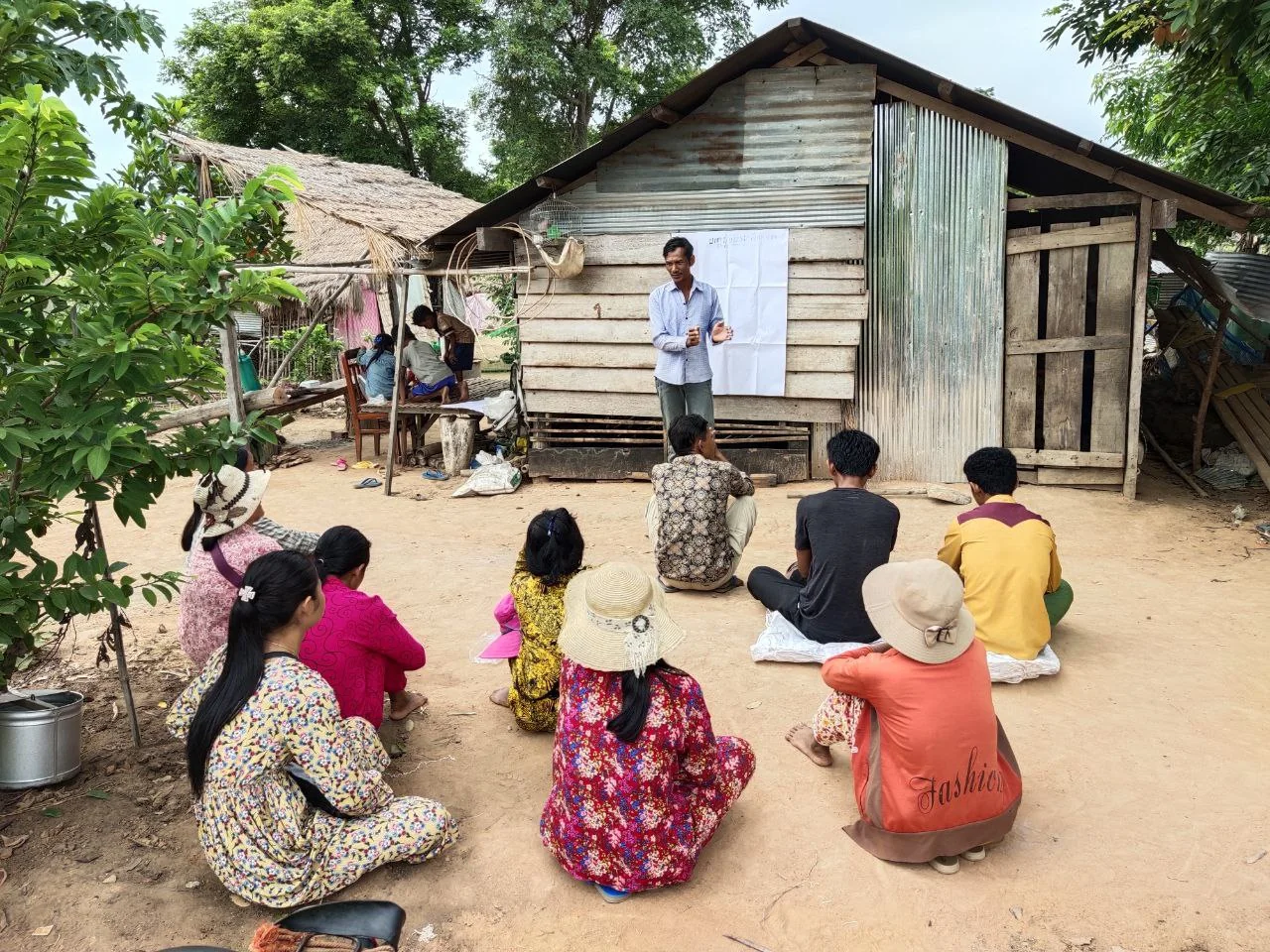 Women and men take part in poultry-management training beside a village home