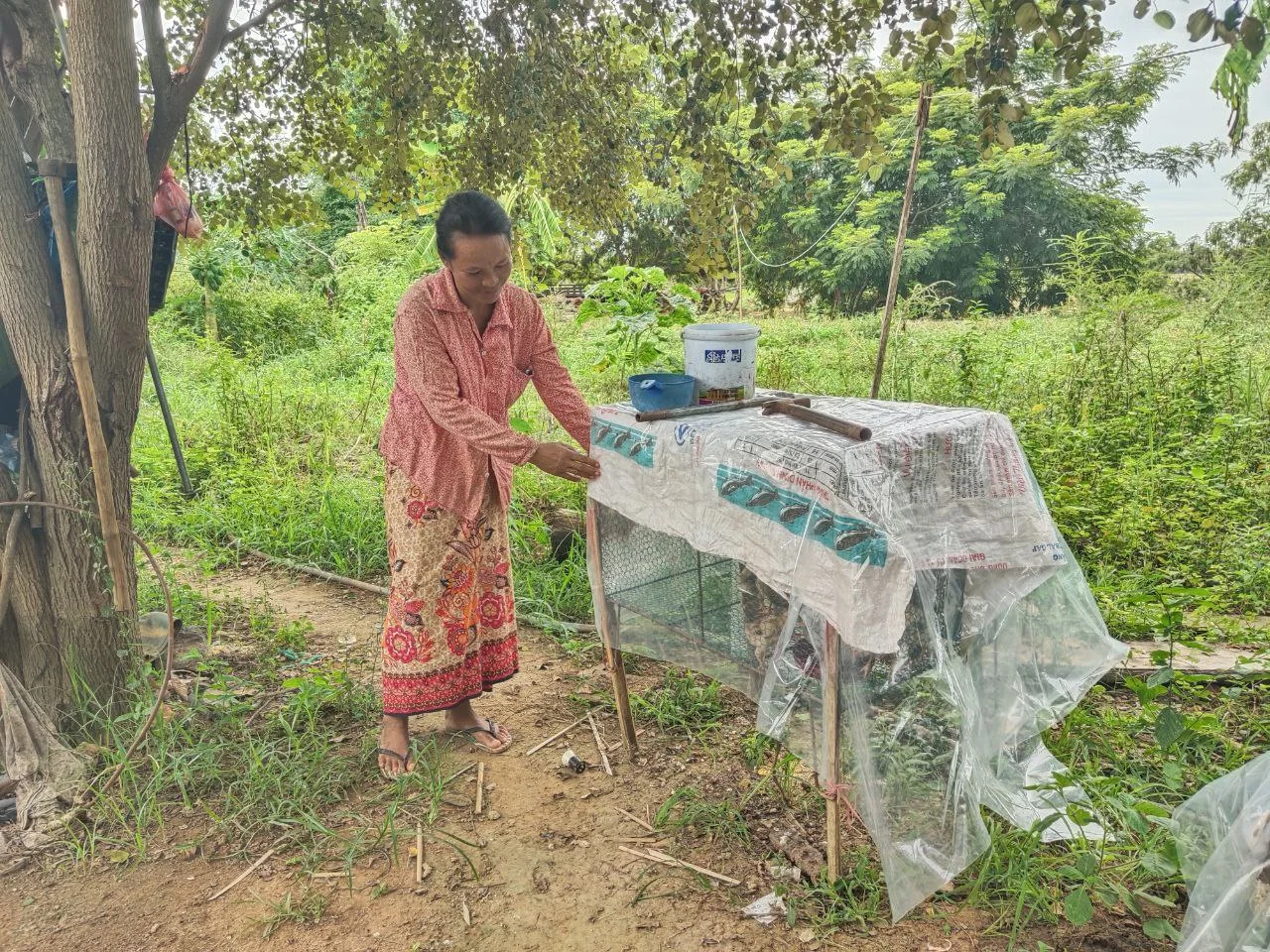A woman stands beside her household poultry-production shelter